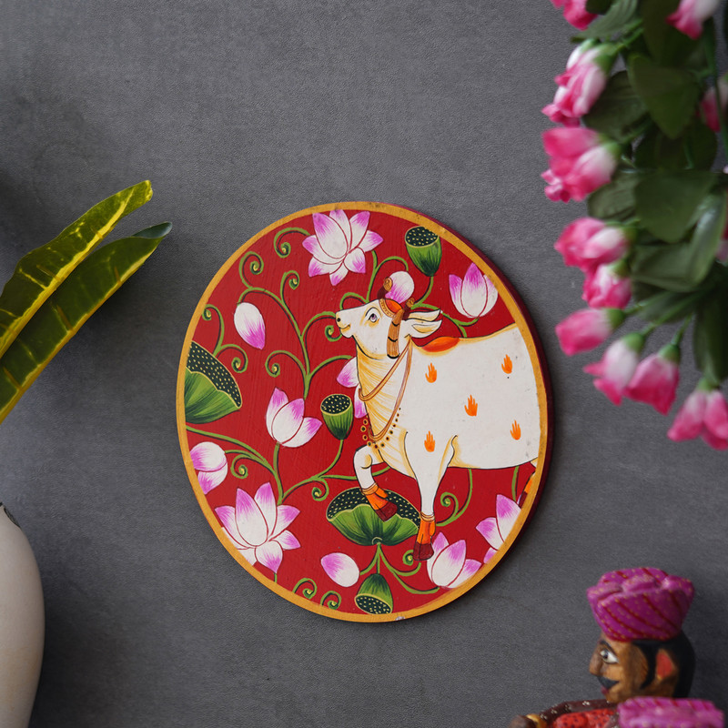 Traditional Pichwai cow painting with lotus flowers — vibrant red backdrop symbolizing devotion and peace.
